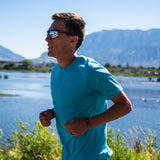 Conner Mantz wearing an ArtiKen bracelet while running outdoors near a lake with mountains in the background.