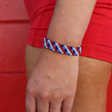 Person wearing a red, white, and blue bracelet on a red background