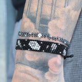 black adjustable beaded bracelet depicting gray and silver comets shooting through a starry sky with a white and gray moon in the center. handmade in Kenya