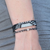 black and gray adjustable bracelet with a white sun depicting a sunset, with a silver moon in the corner. handmade in Kenya