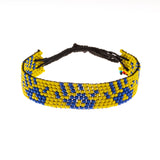 A handmade in Kenya ArtiKen bracelet with a yellow background displays "hands" in blue. 