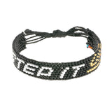 A handmade beaded bracelet from ArtiKen created in Kenya displaying the text Step It Up in white, gold and black.