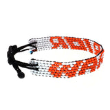 A handmande in Kenya, ArtiKen bracelet displays the word Warrior in orange beads on a white background. 